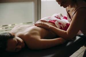 Mit dem Unterarm der Masseurin wird der Unterarm des auf dem Bauch liegenden Gastes massiert bei der Lomi Lomi Massage